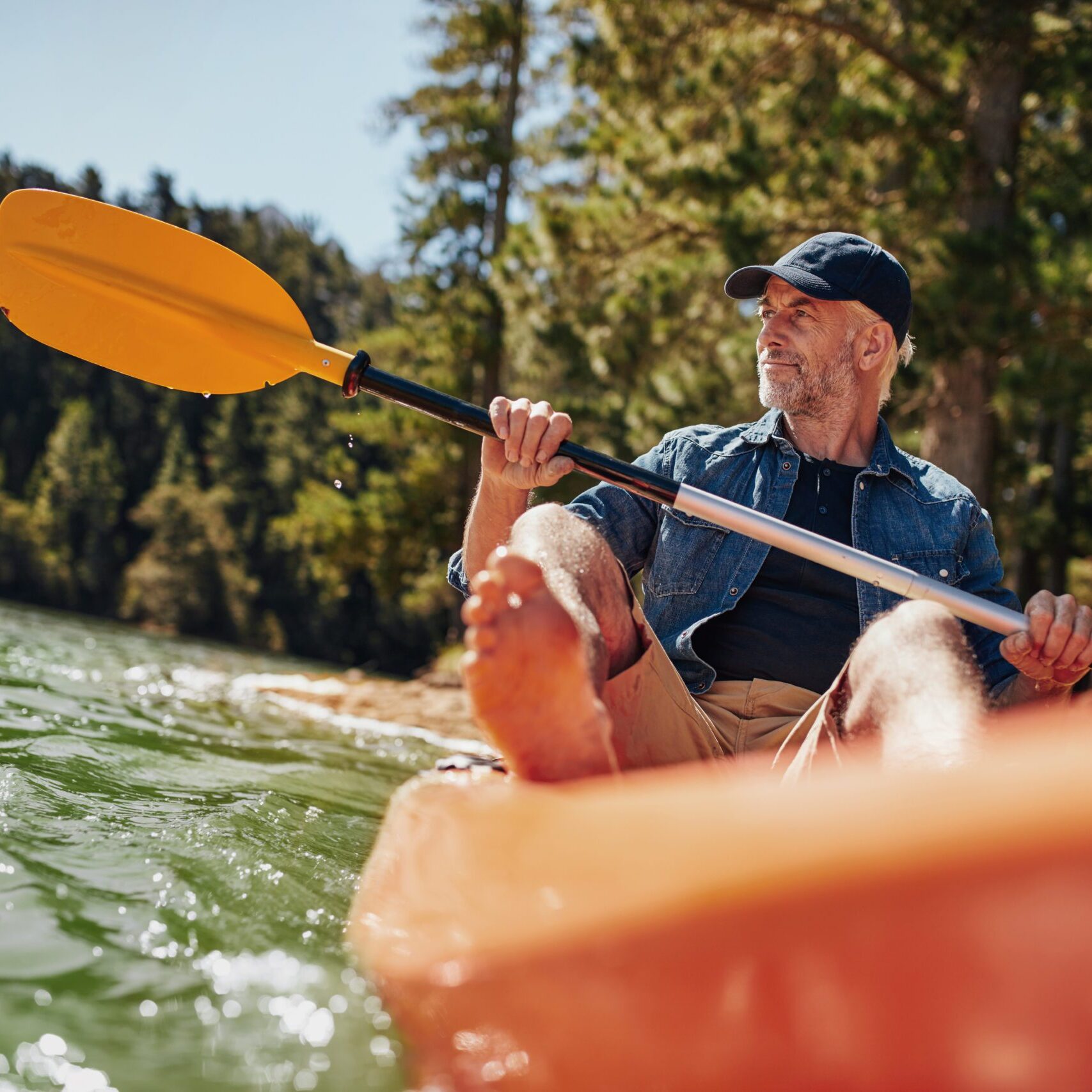 Portrait of a mature man with kayak in a lake. Caucasian man paddling a kayak on summer day.