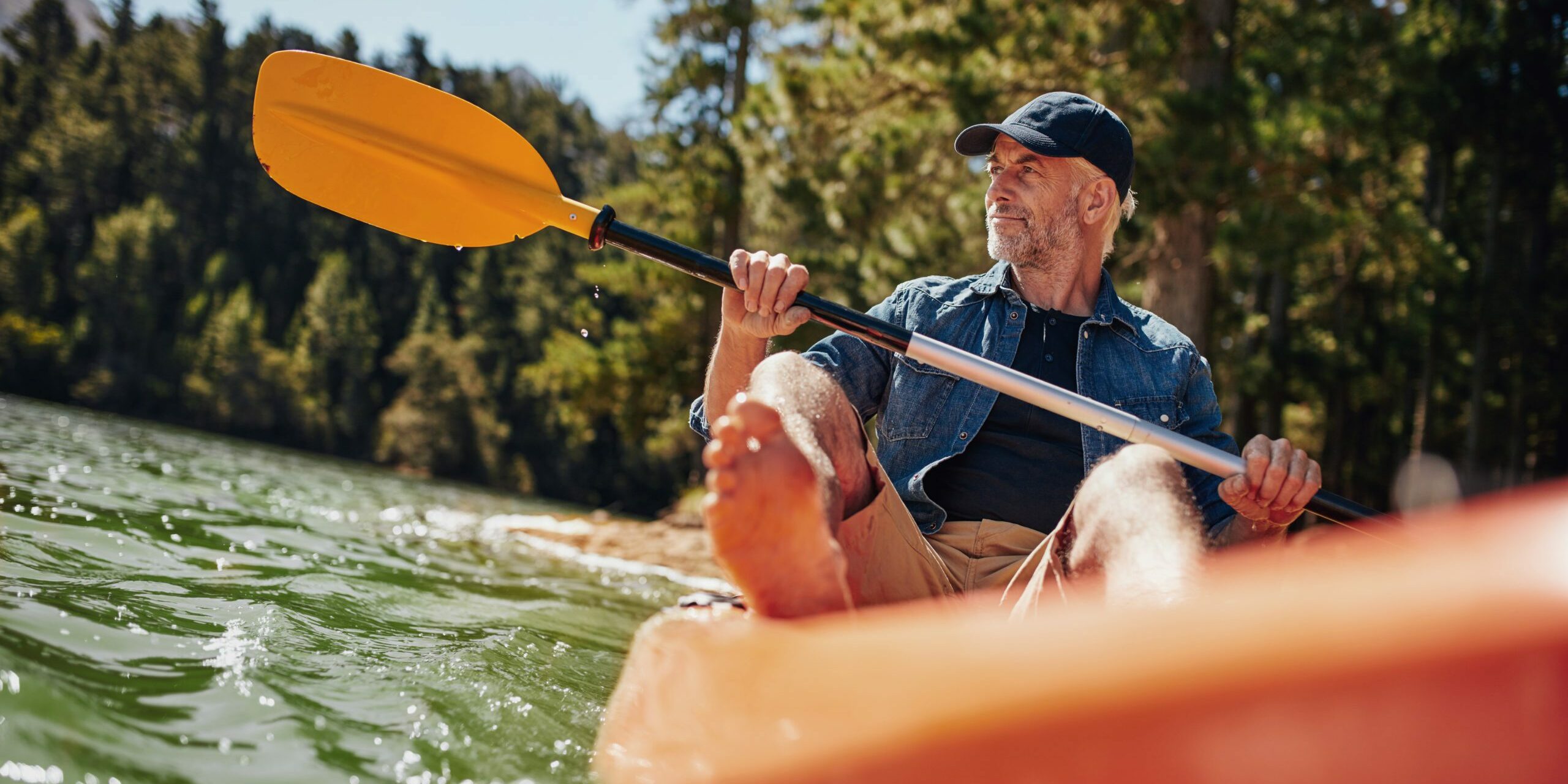 Portrait of a mature man with kayak in a lake. Caucasian man paddling a kayak on summer day.