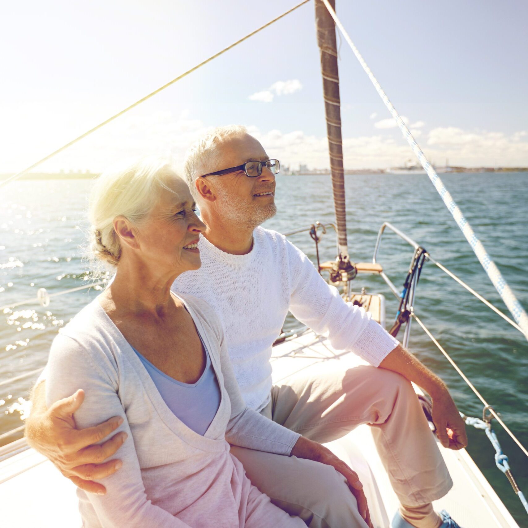 sailing, age, tourism, travel and people concept - happy senior couple hugging on sail boat or yacht deck floating in sea