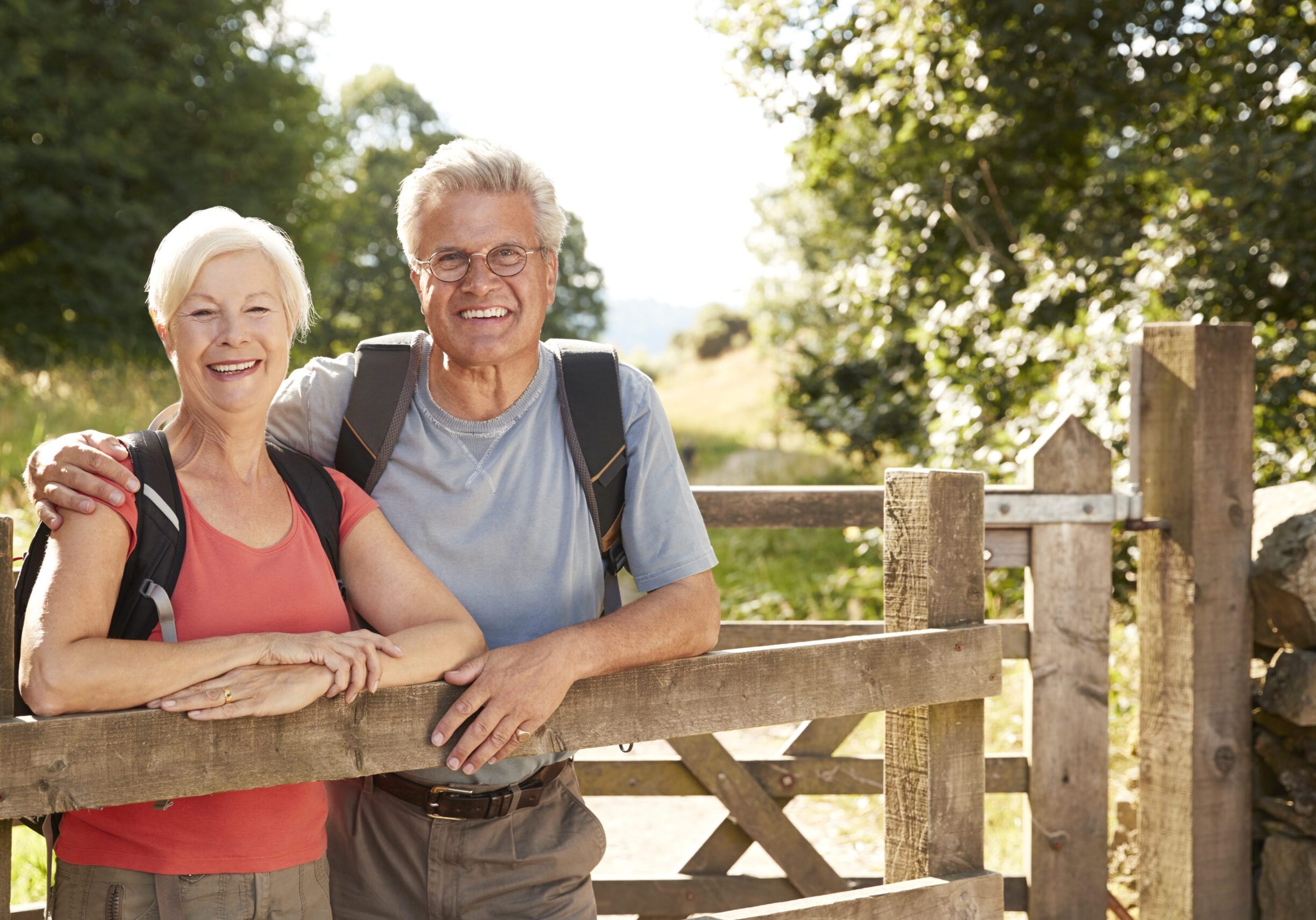 Portrait Of Senior Couple Hiking In Lake District UK Looking Over Wooden Gate