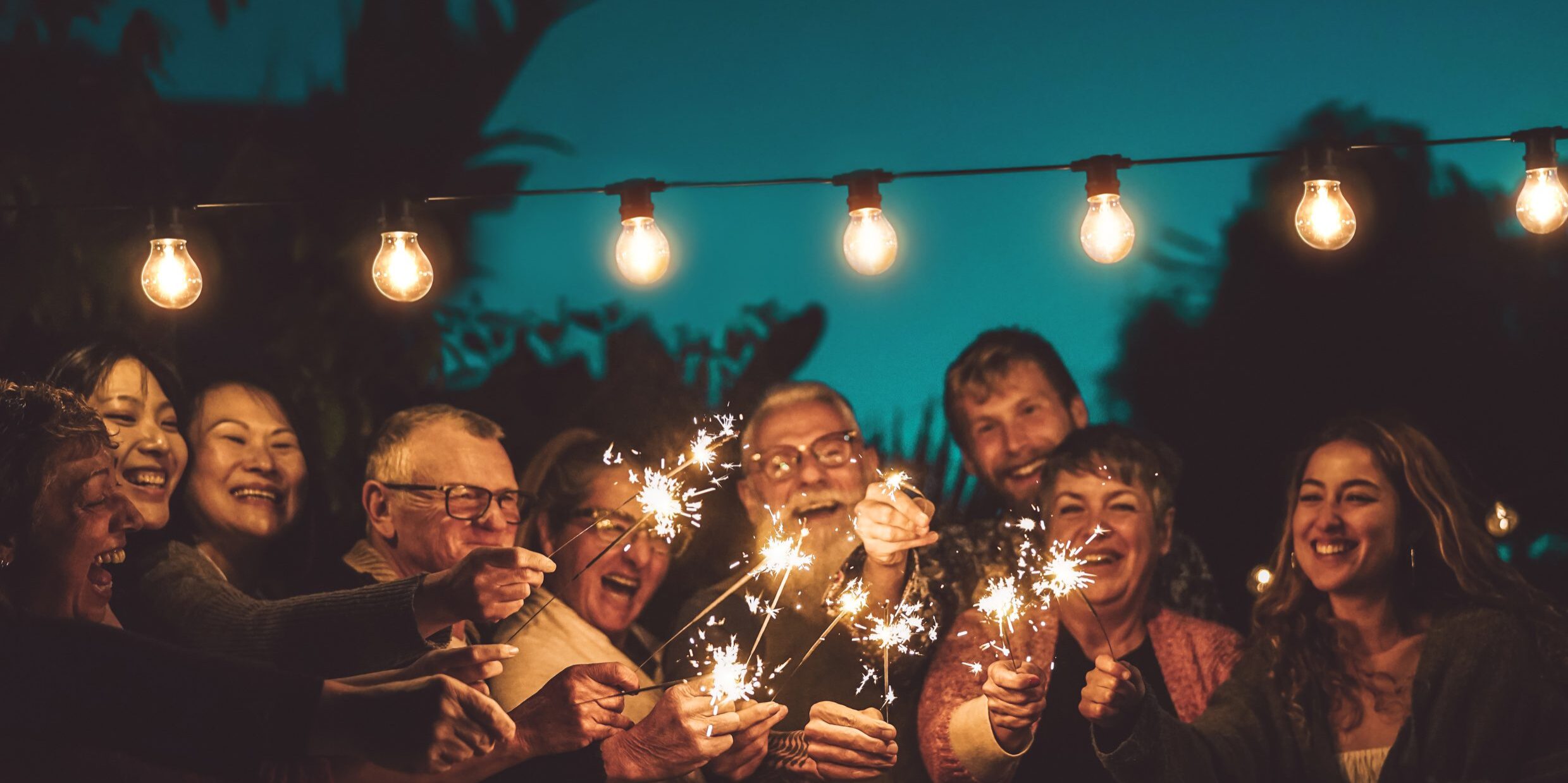 Happy family celebrating with sparkler at night party outdoor - Group of people with different ages and ethnicity having fun together outside - Friendship, eve and celebration concept