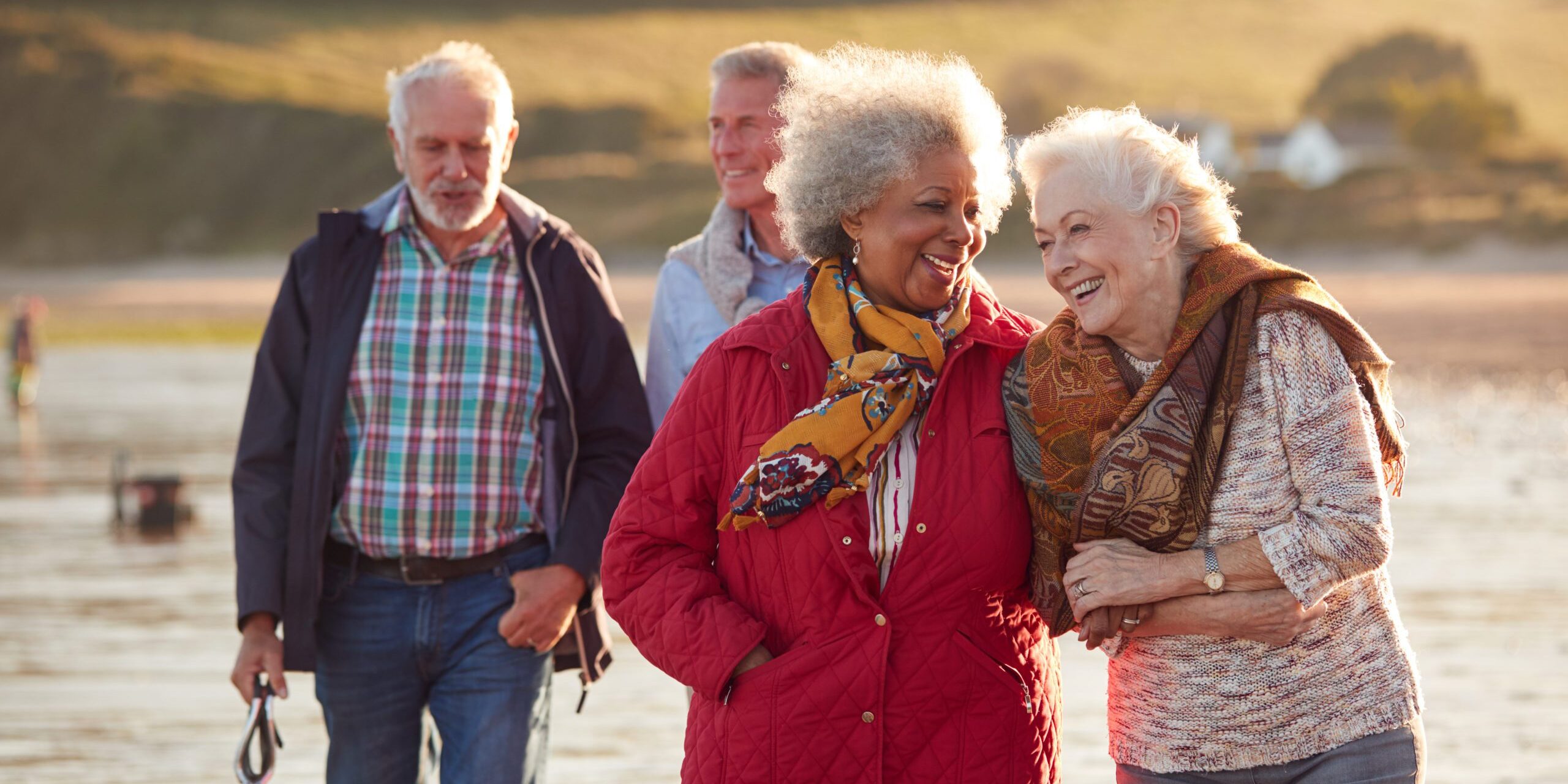 Group Of Smiling Senior Friends Walking Arm In Arm Along Shoreline Of Winter Beach